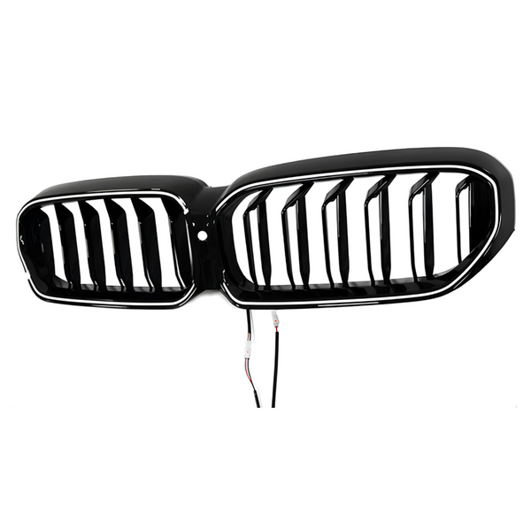 A shiny black car grille with vertical slats is suspended against a plain white background. Two wires dangle below, indicating electrical connectivity for installation.