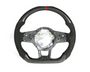 A carbon-fiber steering wheel with a red stripe at the top and a partially exposed interior mechanism, displayed against a plain white background.