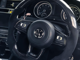 A car steering wheel with a Volkswagen logo, featuring control buttons, is set in a vehicle interior with visible speedometer and climate control dials.