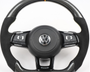 Steering wheel with carbon fiber accents and VW logo, featuring multi-function buttons for control. It rests against a plain white background.