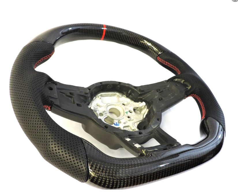 A perforated black steering wheel with red stitching and a central metallic hub is positioned on a white background, highlighting its sporty design and carbon fiber texture.
