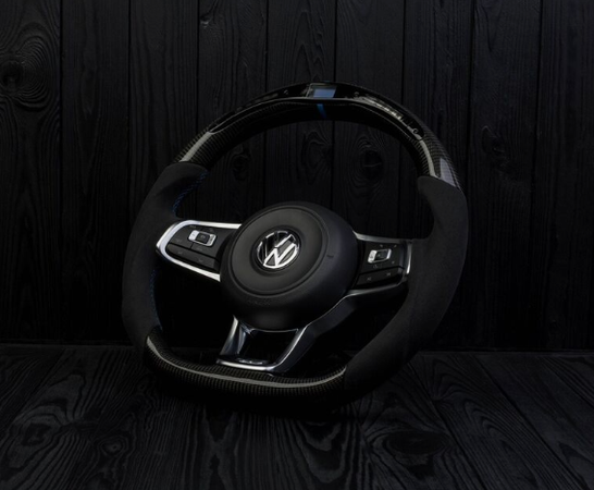 A Volkswagen steering wheel, featuring buttons and a sleek design, rests against a dark, textured wooden backdrop.