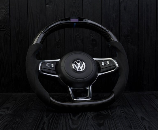 A Volkswagen steering wheel sits upright, displaying buttons on its arms, against a dark wooden background.