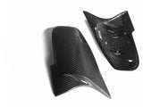 Two carbon fiber car mirror covers rest side by side on a white surface. The right cover shows the interior structure with mounting clips visible.