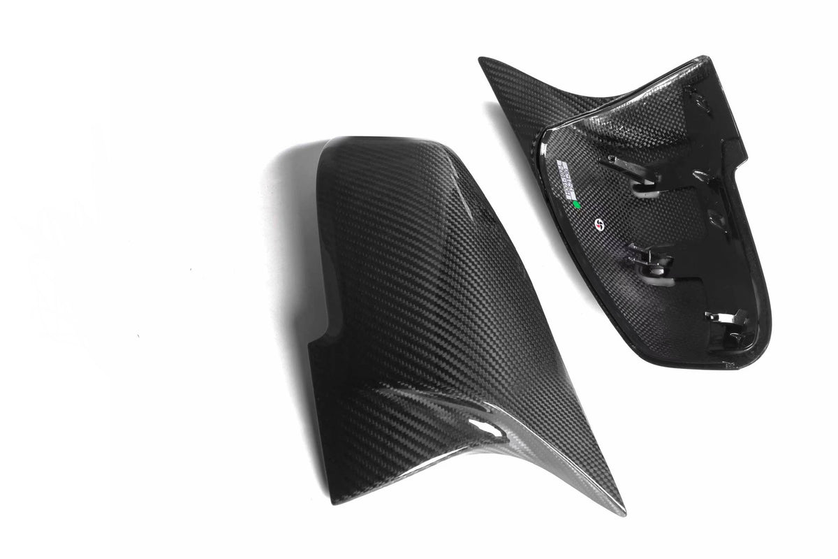 Two carbon fiber car mirror covers rest side by side on a white surface. The right cover shows the interior structure with mounting clips visible.