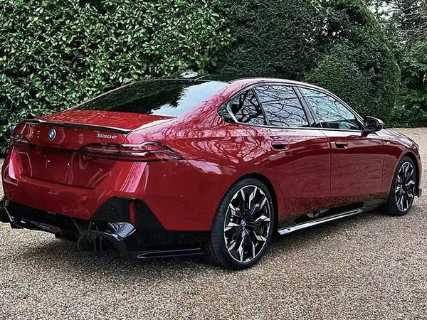 A red BMW 530e is parked on a gravel surface, surrounded by lush greenery. The car's sleek design and shiny wheels stand out.
