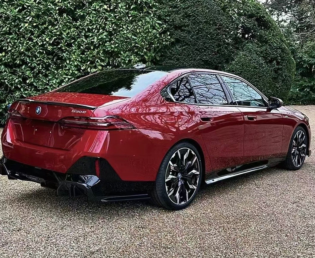 A red BMW 530e is parked on a gravel surface, surrounded by lush greenery. The car's sleek design and shiny wheels stand out.