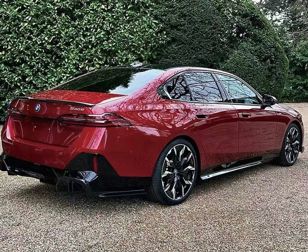 A red BMW 530e is parked on a gravel surface, surrounded by lush greenery. The car's sleek design and shiny wheels stand out.