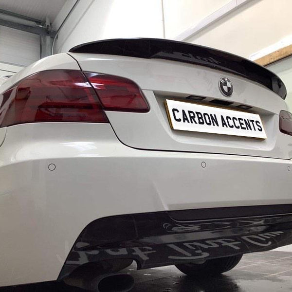 Car with modified rear, including darkened tail lights and carbon fiber accents, parked indoors. The license plate reads, "CARBON ACCENTS." Workshop tools and supplies are visible on shelves.