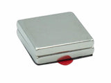 A square silver magnet presses against a flat surface, with a small red tab protruding. The background is plain white, emphasizing the magnet's metallic sheen and compact size.