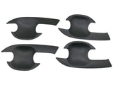 Four black, curved, plastic car door handle covers are positioned symmetrically on a plain background. They have an ergonomic design with cutouts for easy installation.