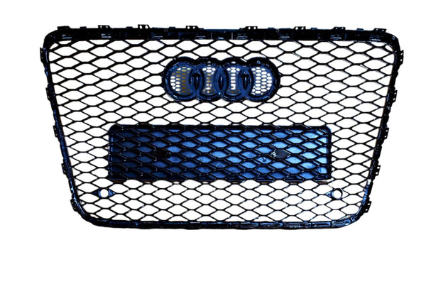 A black honeycomb car grille with the Audi logo prominently displayed, featuring four interlocking rings. The grille is set against a plain white background.