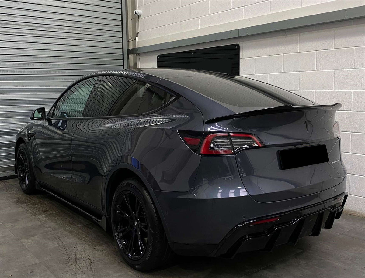 A sleek, dark-colored car is parked in a garage beside a metallic shutter. The car's glossy surface reflects the surroundings.