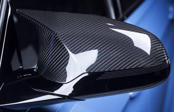 A carbon fiber car side mirror reflects light, showcasing its glossy surface and detailed texture. It is attached to a sleek, blue vehicle, emphasizing a modern, high-performance design.