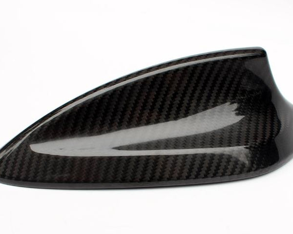 A shark fin-shaped car antenna made from carbon fiber, resting on a white surface. It features a glossy finish and a sleek, aerodynamic design.