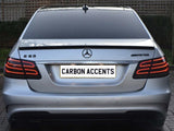 The image shows the rear of a silver Mercedes-Benz E63 AMG with illuminated tail lights, parked on a brick driveway. The license plate reads 