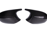 Two glossy carbon fiber mirror covers facing each other, exhibiting curved shapes and smooth surfaces, set against a plain white background.