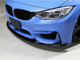 A blue sports car, with a carbon fiber front splitter and detailed headlights, is parked in a garage. The floor is marked with 