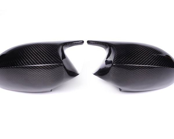 Two black carbon fiber car mirror covers face each other, resting on a plain white background, highlighting their glossy texture and sleek design.