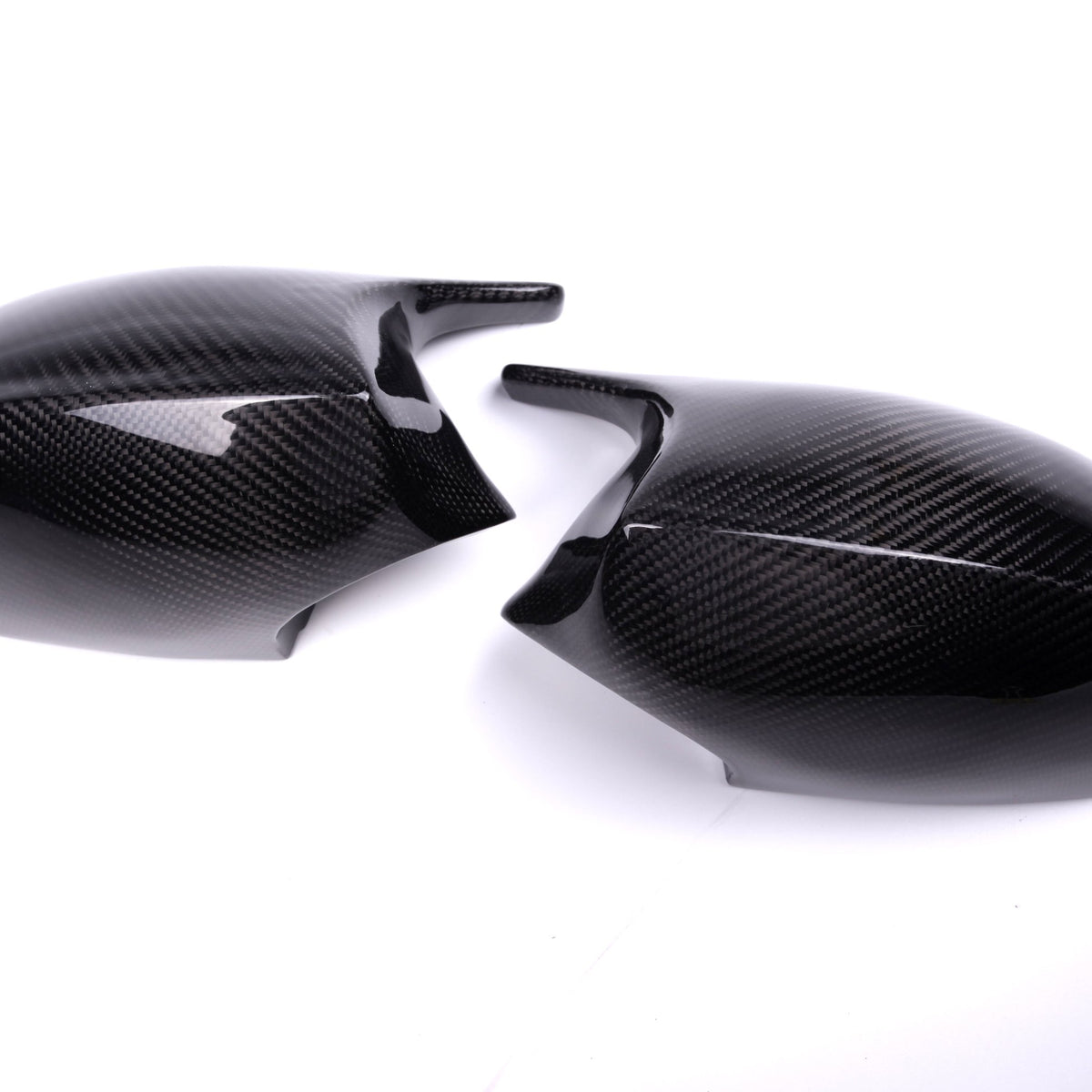 Two carbon fiber mirror caps rest on a white surface, featuring a glossy finish and textured pattern, suggesting use in automotive applications.