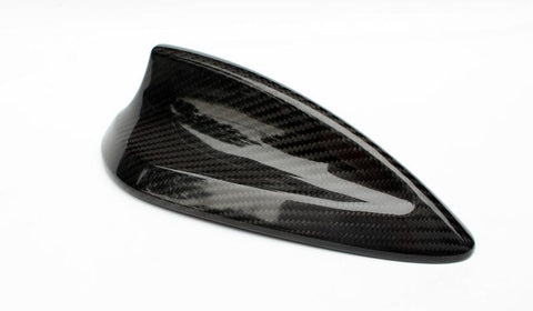 A sleek, black carbon-fiber car antenna rests on a white surface, showcasing a streamlined, shark-fin design that reflects light, highlighting its glossy texture and modern aesthetics.