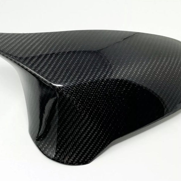 A smooth, glossy carbon fiber piece rests against a plain white background, showcasing its sleek, curved design and textured pattern, likely used as a protective cover or aerodynamic component.