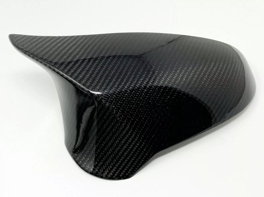 A glossy carbon fiber car mirror cap with a sleek, curved design, rests on a plain white background, showing its textured surface.
