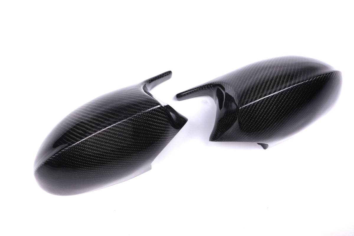 Two carbon fiber car side mirror covers lie on a white surface, displaying a sleek, glossy texture and a subtle weave pattern.