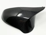 A smooth, black carbon fiber car mirror cover with a glossy finish is resting on a plain white surface, highlighting its sleek design and reflective texture.