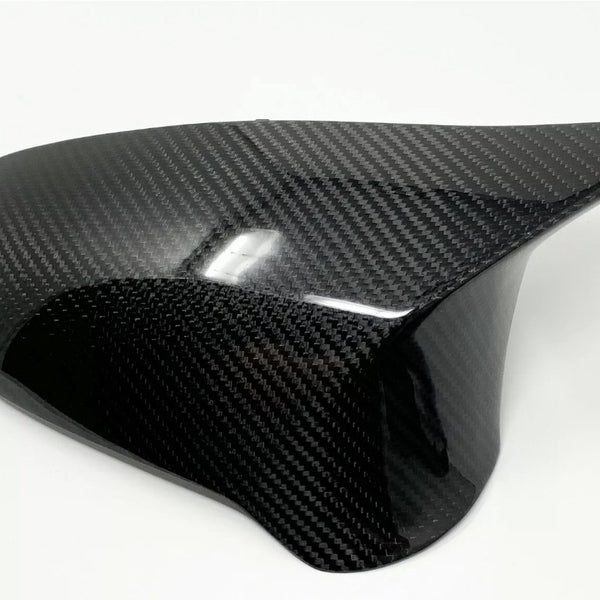 A smooth, black carbon fiber car mirror cover with a glossy finish is resting on a plain white surface, highlighting its sleek design and reflective texture.