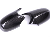 Two glossy carbon fiber mirror covers, resting on a white background, feature a distinctive woven texture and sleek contours.