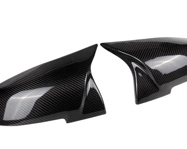 Two glossy carbon fiber side mirror covers rest adjacent, reflecting light and featuring a distinct weaved pattern; placed against a plain white background.