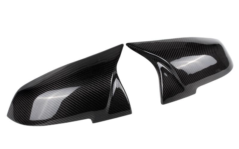 Two glossy carbon fiber side mirror covers rest adjacent, reflecting light and featuring a distinct weaved pattern; placed against a plain white background.