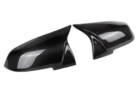 Two glossy carbon fiber side mirror covers rest adjacent, reflecting light and featuring a distinct weaved pattern; placed against a plain white background.