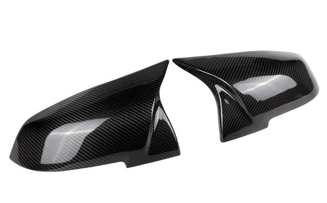Two sleek, carbon fiber side mirror covers are angled toward each other, showcasing a reflective surface and intricate weave pattern against a plain white background.