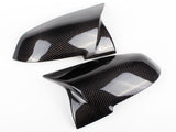 Two glossy carbon fiber side mirror covers rest on a clean white surface, showcasing their sleek, aerodynamic design.