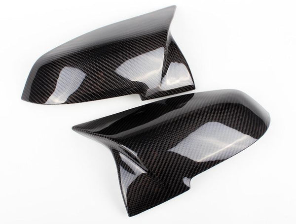 Two glossy carbon fiber side mirror covers rest on a clean white surface, showcasing their sleek, aerodynamic design.