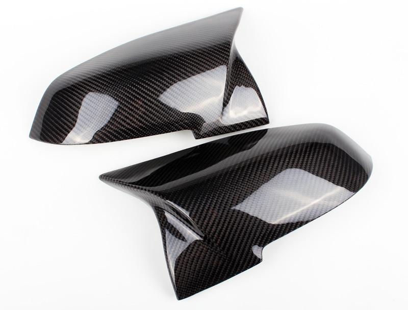 Two sleek carbon fiber car mirror covers, polished and shiny, rest on a plain white background, displaying a reflective surface with a distinctive checkered pattern.