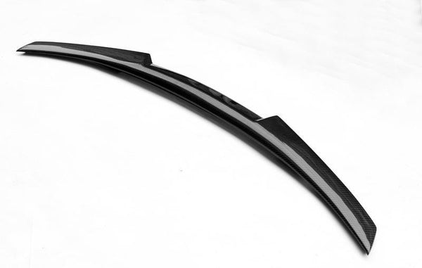 Carbon fiber car spoiler rests on a plain white surface. Its smooth, sleek design features a curved, aerodynamic shape, highlighting its purpose in enhancing vehicle performance and appearance.
