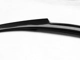 A sleek carbon fiber car spoiler, featuring a glossy finish, rests on a plain white background, highlighting its aerodynamic curve and textured surface.