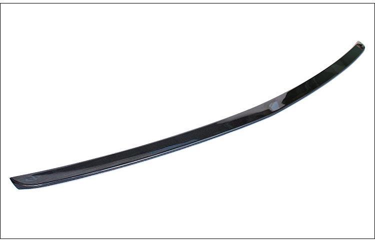A sleek, curved carbon fiber spoiler lies on a plain white background. The spoiler's glossy surface reflects light, highlighting its aerodynamic design.
