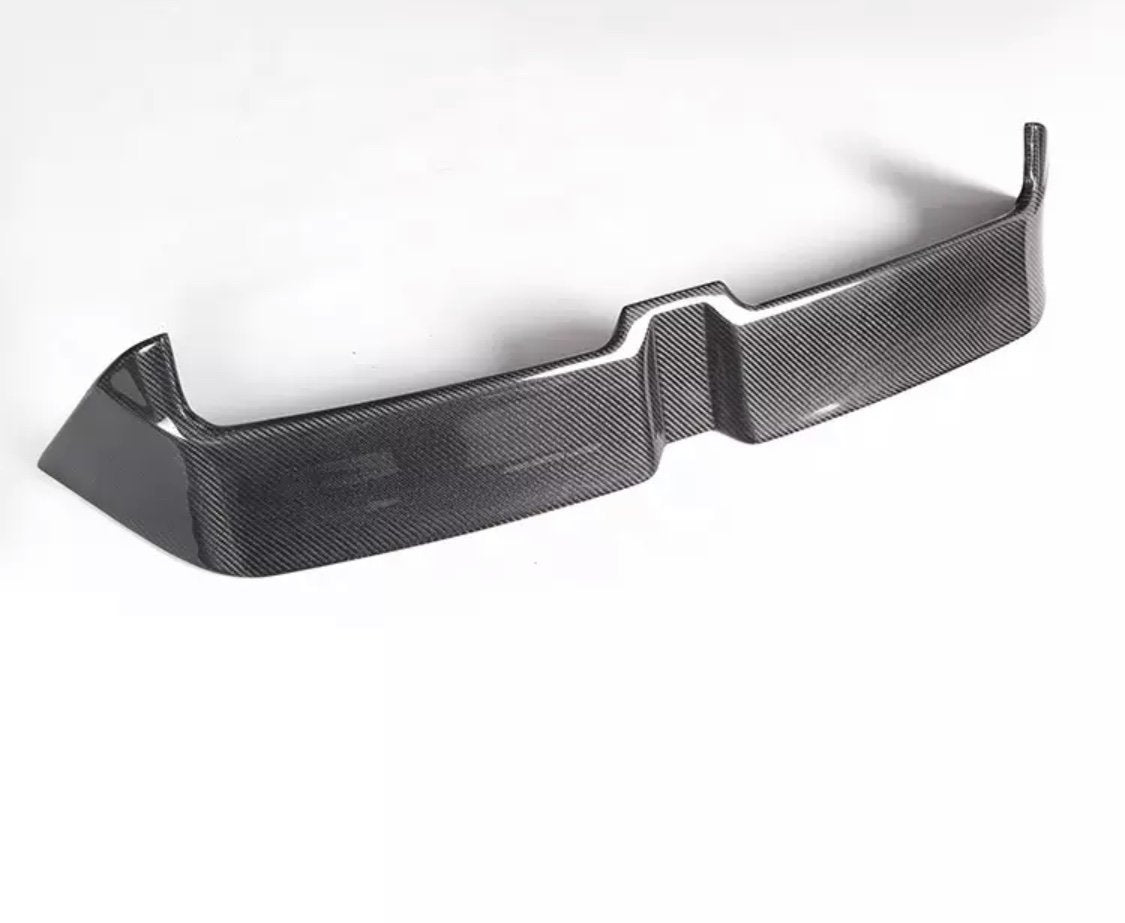 A carbon fiber car bumper sits on a white background, showcasing a sleek, angular design with a textured surface and raised edges.