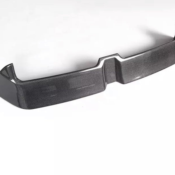 A carbon fiber car bumper sits on a white background, showcasing a sleek, angular design with a textured surface and raised edges.