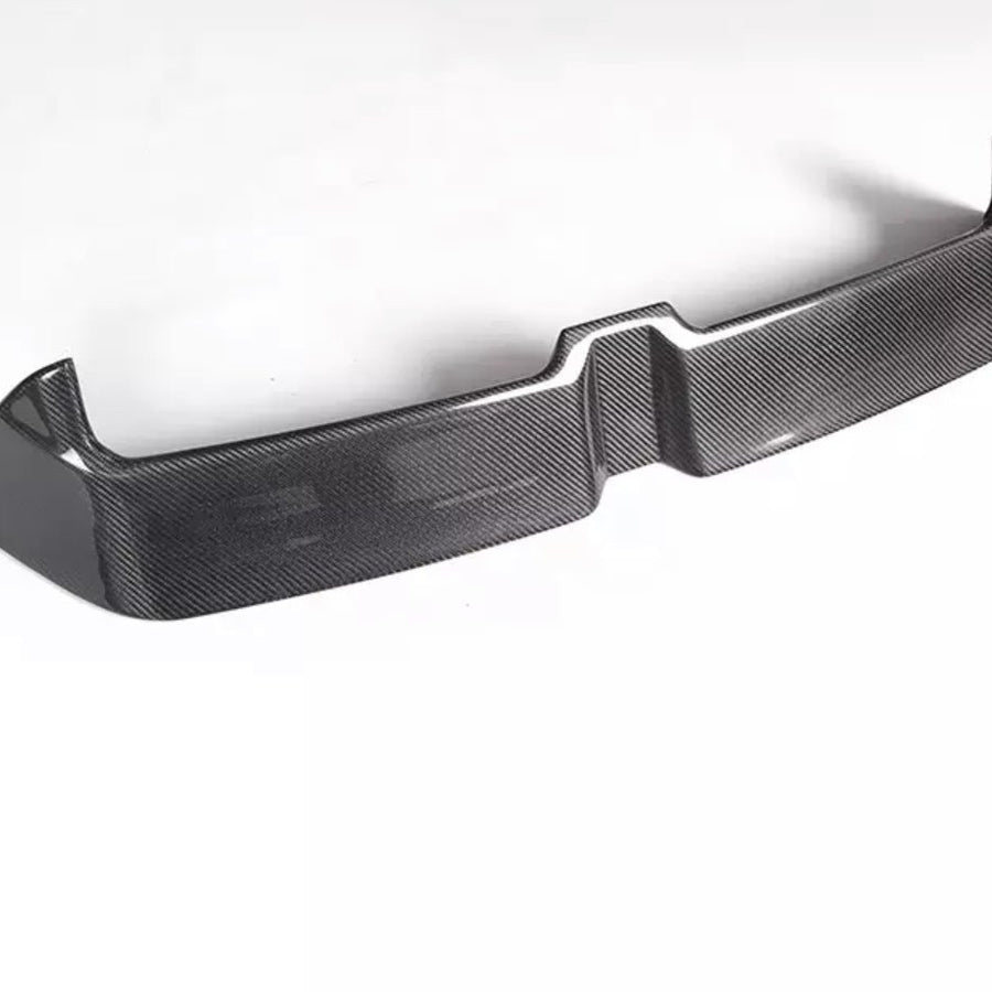 A carbon fiber car bumper sits on a white background, showcasing a sleek, angular design with a textured surface and raised edges.