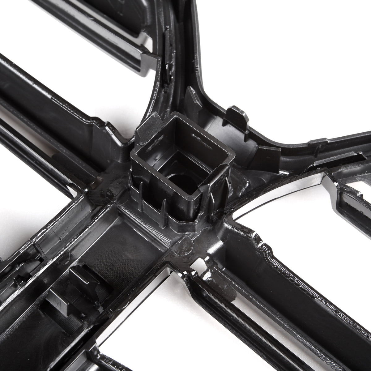 A black plastic grid structure sits on a white background, featuring intersecting lines with a central square cavity, likely part of an automotive or industrial component.
