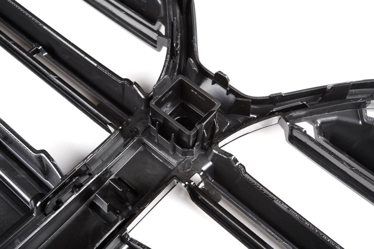 A black plastic grid structure sits on a white background, featuring intersecting lines with a central square cavity, likely part of an automotive or industrial component.