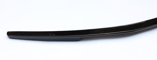 A sleek, elongated carbon fiber object rests motionless against a plain white background, highlighting its smooth surface and subtle curvature.