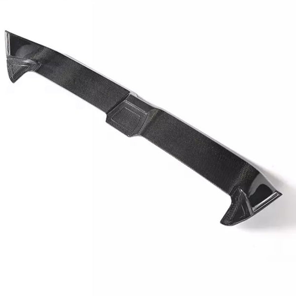 A carbon fiber car spoiler lies on a plain white background, highlighting its aerodynamic shape and texture.
