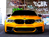 A bright yellow sports car, parked stationary, faces forward. It is under a graffiti-covered bridge, with colorful urban artwork like 