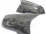Two dark, carbon fiber car side mirrors rest on a white surface, showcasing a sleek, glossy finish with visible fiber patterns.